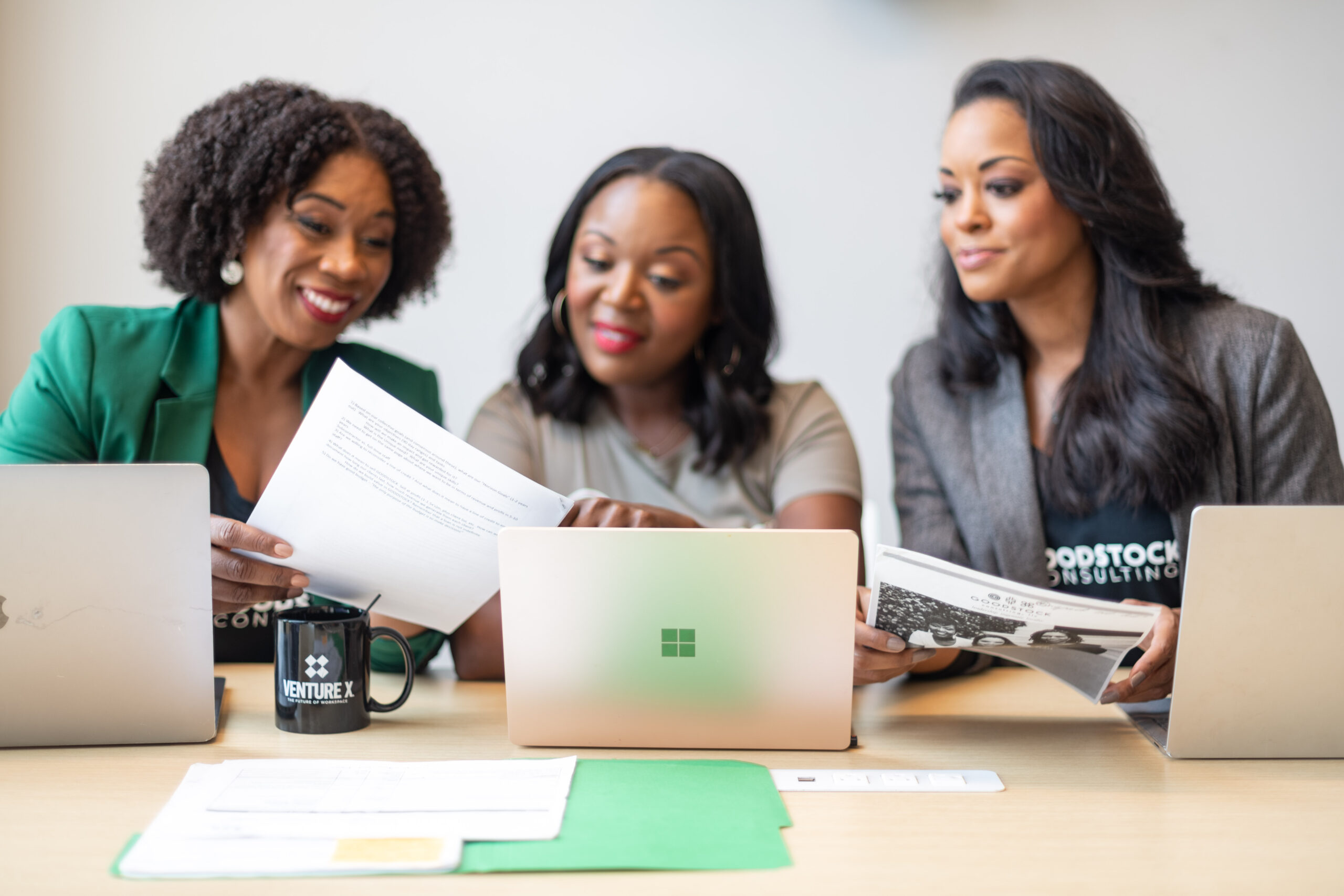 Three black business women looking at some paperwork with their computers in front of them.